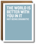 A greeting card with a light blue background and bold white text reading 'THE WORLD IS BETTER WITH YOU IN IT NOT BEING DRAMATIC,' shown with a brown kraft envelope behind it on a white background.