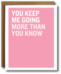 A pink greeting card with bold white text reading 'YOU KEEP ME GOING MORE THAN YOU KNOW' and a brown envelope behind it on a white background.