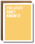 A yellow greeting card with bold white text reading 'I'M LUCKY AND I KNOW IT' stacked vertically, shown with a brown envelope behind it on a white background.
