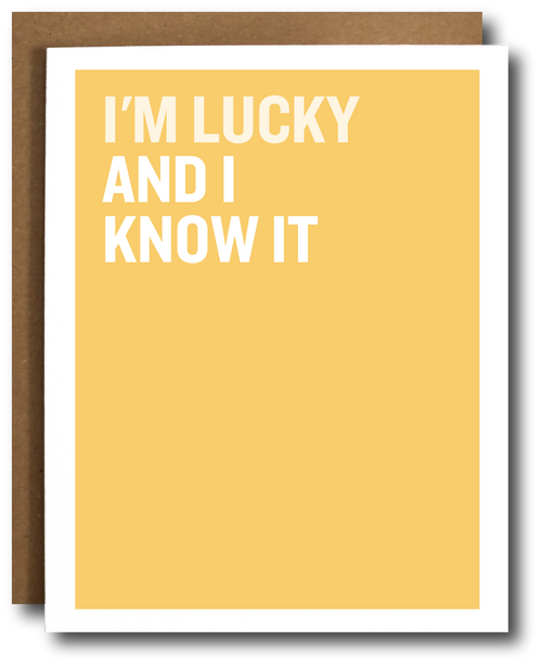 A yellow greeting card with bold white text reading 'I'M LUCKY AND I KNOW IT' stacked vertically, shown with a brown envelope behind it on a white background.