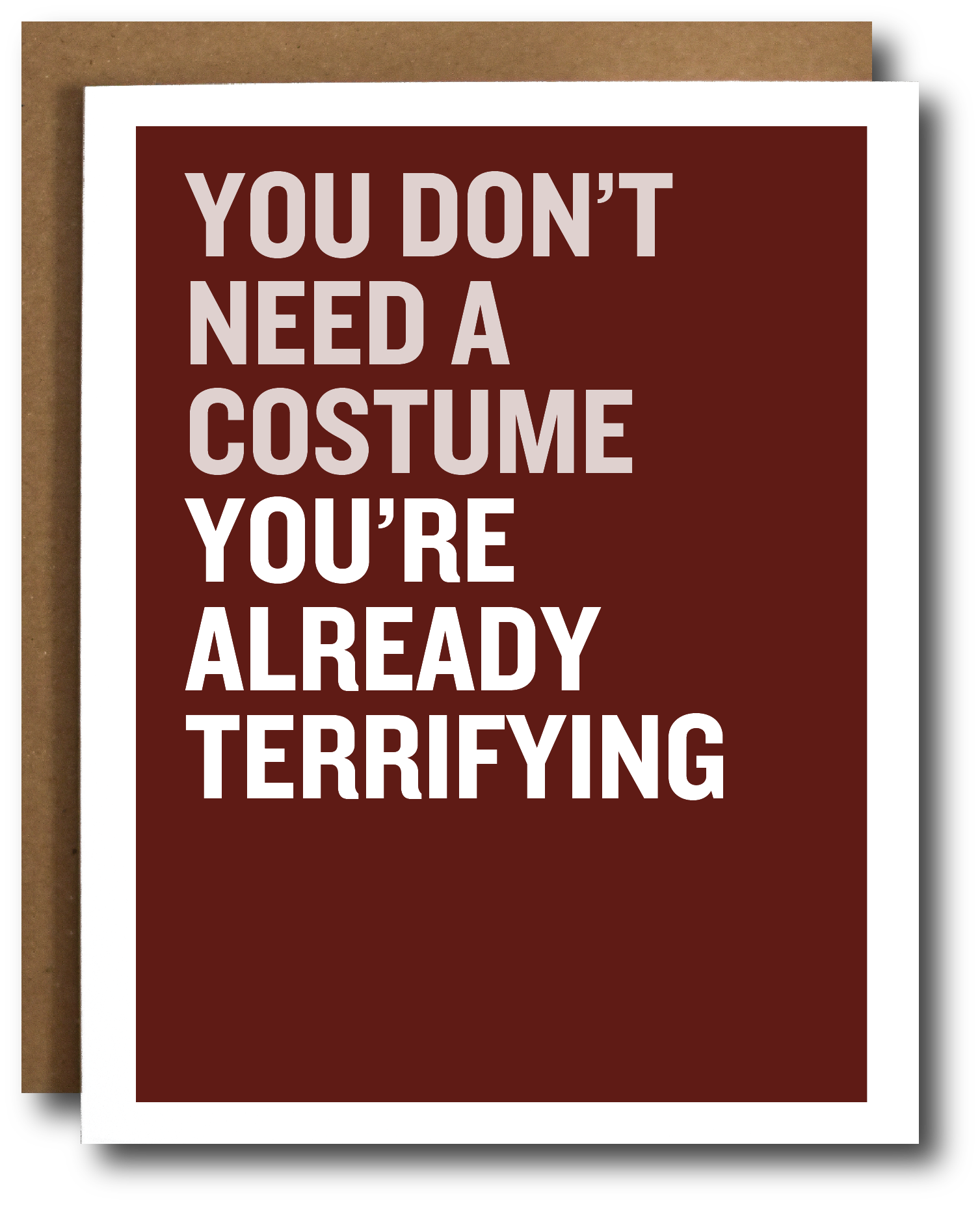 A greeting card with a dark red background and bold white text reading 'YOU DON'T NEED A COSTUME YOU'RE ALREADY TERRIFYING', shown with a brown kraft envelope behind it on a white background.