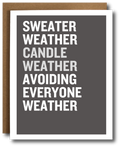 A greeting card with a dark gray face and bold white text reading 'SWEATER WEATHER CANDLE WEATHER AVOIDING EVERYONE WEATHER,' shown with a brown kraft envelope behind it on a white background.