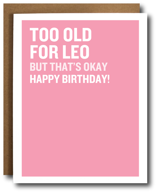 A pink greeting card with bold white text reading 'TOO OLD FOR LEO BUT THAT'S OKAY HAPPY BIRTHDAY!' shown with a brown envelope behind it on a white background.