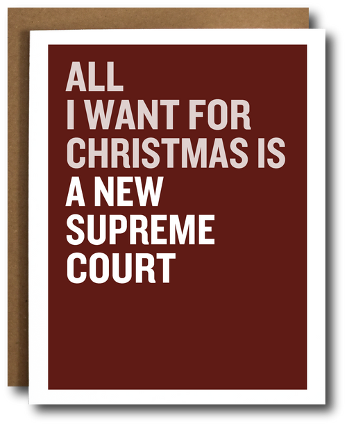 A greeting card with a dark red background and bold white text reading 'ALL I WANT FOR CHRISTMAS IS A NEW SUPREME COURT,' shown with a brown envelope behind it on a white background.