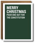 A dark green Christmas greeting card with bold white text reading 'MERRY CHRISTMAS POUR ONE OUT FOR THE CONSTITUTION', shown with a brown kraft envelope behind it on a white background.