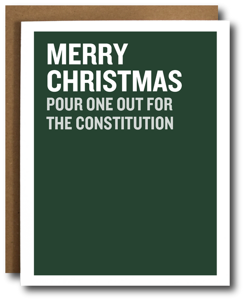 A dark green Christmas greeting card with bold white text reading 'MERRY CHRISTMAS POUR ONE OUT FOR THE CONSTITUTION', shown with a brown kraft envelope behind it on a white background.