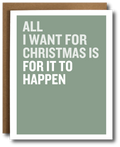 A greeting card with a sage green background and bold white text reading 'ALL I WANT FOR CHRISTMAS IS FOR IT TO HAPPEN,' shown with a brown kraft envelope behind it on a white background.