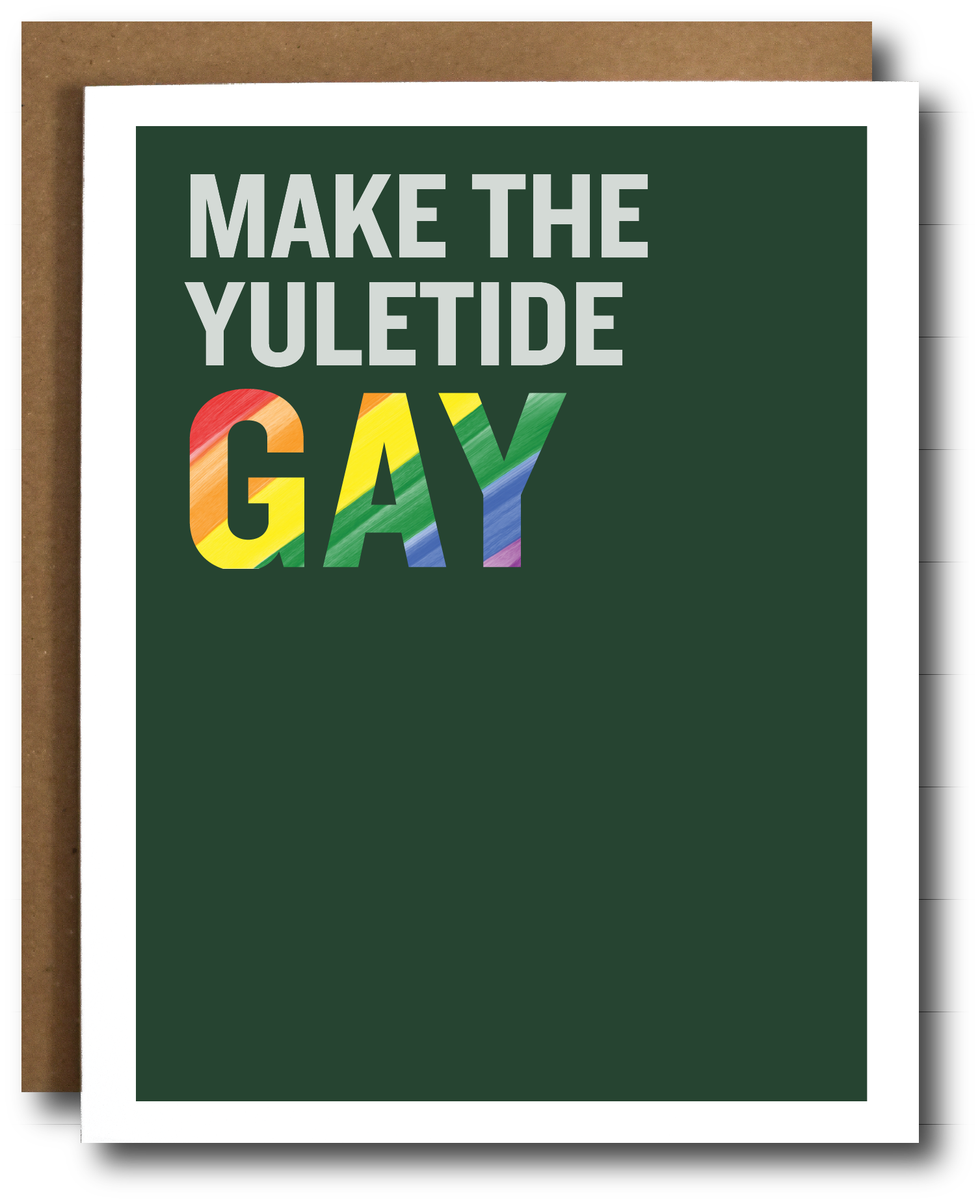 A greeting card with a dark green background and the text 'MAKE THE YULETIDE GAY' in white and rainbow-striped letters, shown with a brown kraft envelope behind it on a white background.