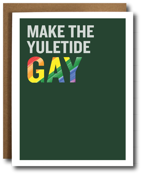A greeting card with a dark green background and the text 'MAKE THE YULETIDE GAY' in white and rainbow-striped letters, shown with a brown kraft envelope behind it on a white background.