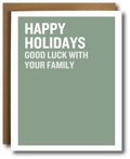 A holiday greeting card with a sage green background and bold white text reading 'HAPPY HOLIDAYS GOOD LUCK WITH YOUR FAMILY,' shown with a brown envelope behind it on a white background.
