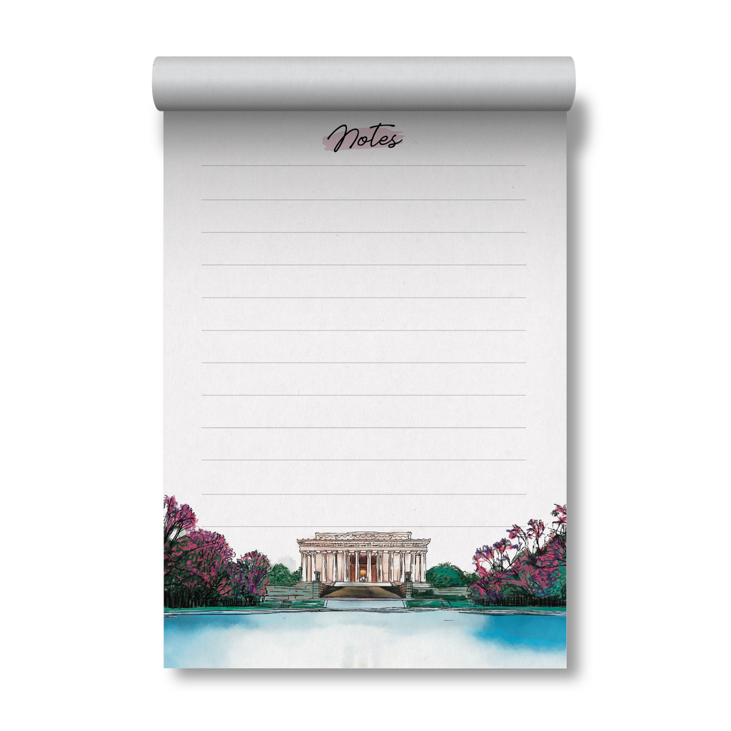 A vertical desk notepad with a rolled top, featuring lined writing space and the word 'Notes' at the top, with a watercolor illustration of the Lincoln Memorial and pink flowering trees along the bottom.